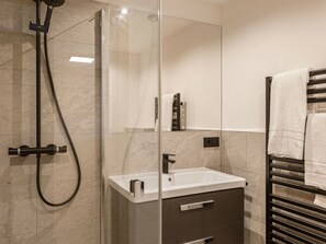 Casa de banho moderna com cabine de duche em vidro, lavatório branco e porta-toalhas.