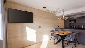 Una cocina moderna con armarios de madera, un comedor con mesa y sillas de madera, y un televisor de pantalla plana grande montado en la pared.