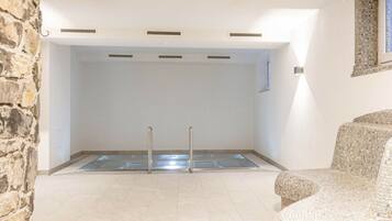 A room with a pool, stone wall, and a green exit sign.