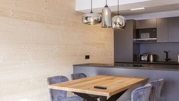 A modern kitchen with a wooden island, pendant lighting, and grey upholstered chairs.