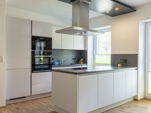 A modern kitchen with a central island, built-in oven, and stainless steel appliances.