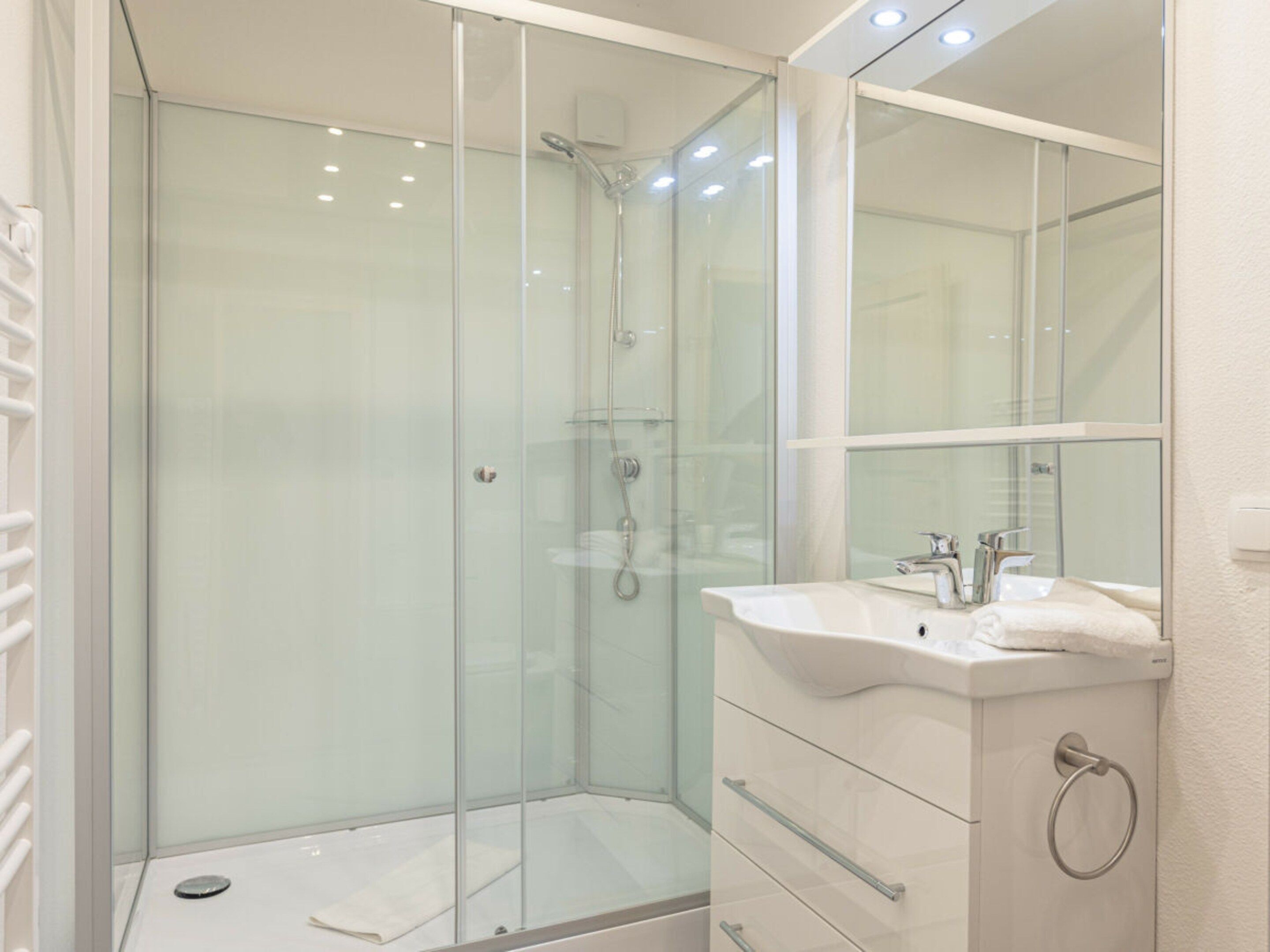 A modern bathroom with a glass shower enclosure, a white sink, and a mirror above the vanity.