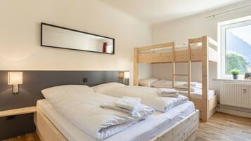 Habitación de hotel con literas, una cama individual, una mesita de noche con lámpara y ventana con vistas al exterior.