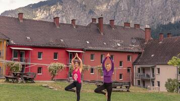 Two individuals practicing yoga outdoors with a mountainous backdrop and residential buildings.