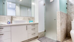 Un bagno con lavandino bianco, uno specchio, cabina doccia in vetro e un water.