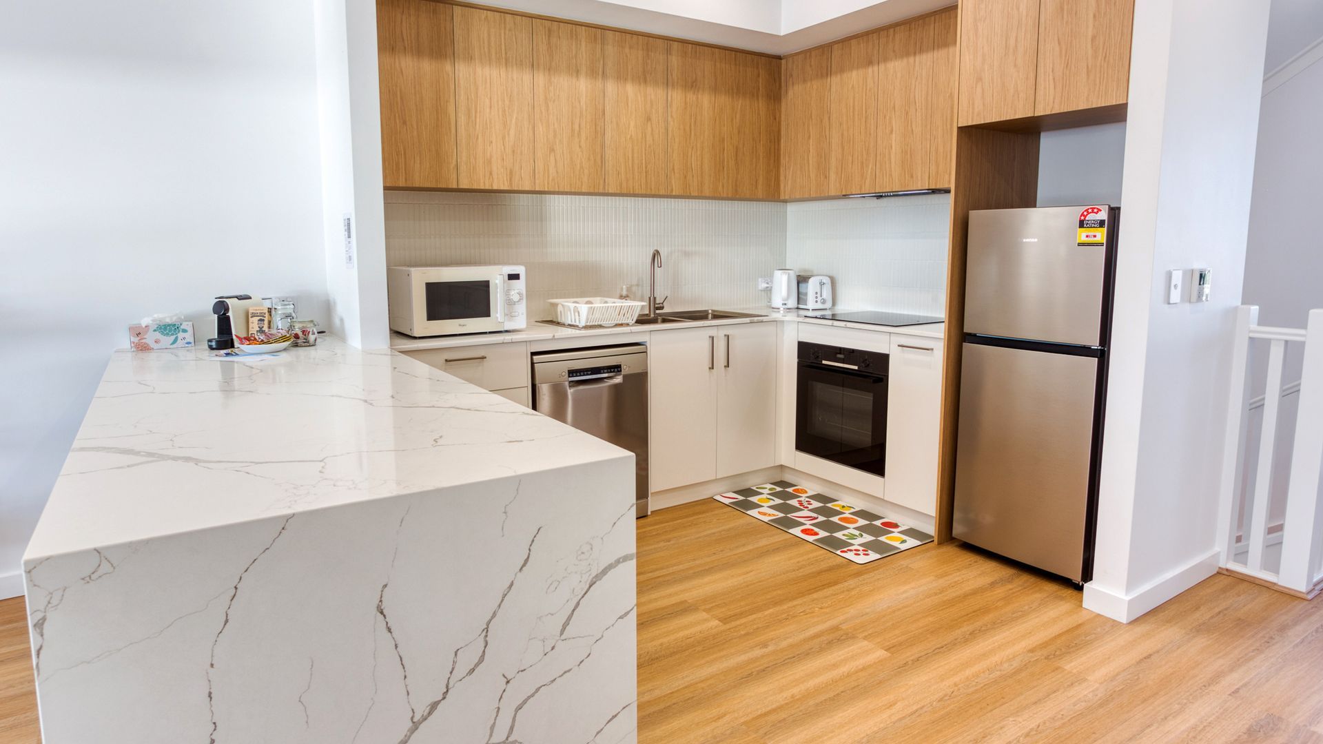 A modern kitchen with white cabinetry, a marble countertop, a stainless steel refrigerator, and a microwave.