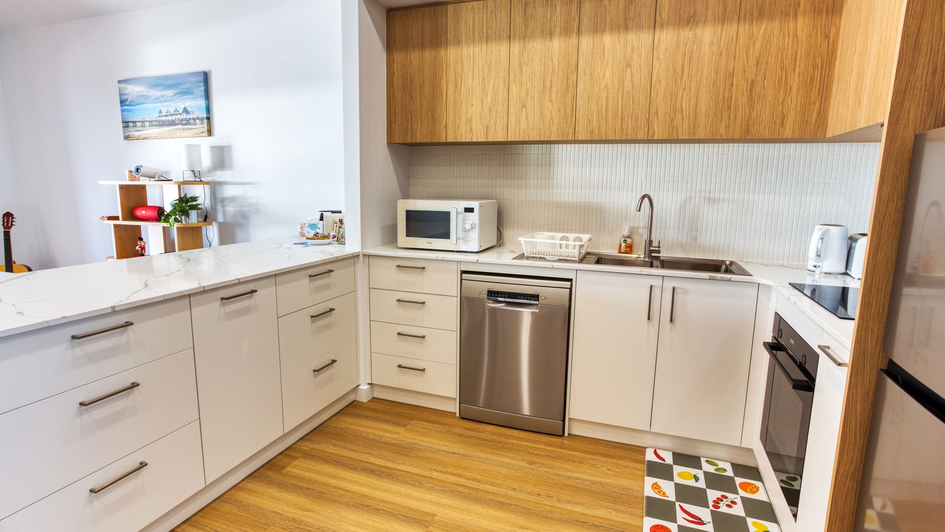 Een moderne keuken met witte kastjes, een roestvrijstalen vaatwasser, een magnetron en een spoelbak.