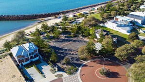 Vista aérea de una propiedad costera con zona de estacionamiento, un edificio de techo azul y una playa al fondo.