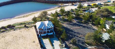 An aerial view of a coastal property with a large building, a parking area, and a beach.