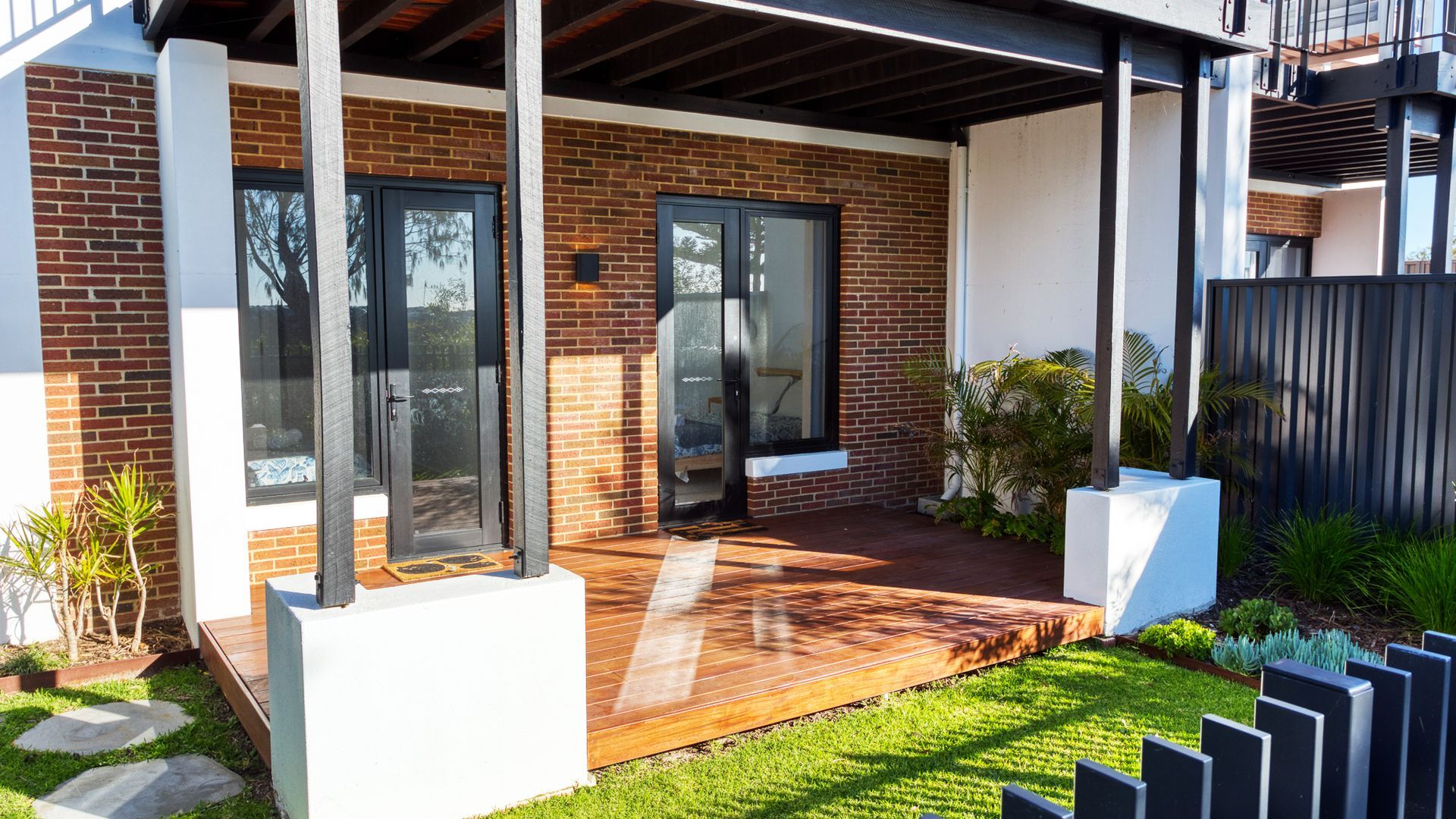 A modern house with a brick exterior, large glass doors, and a wooden deck.