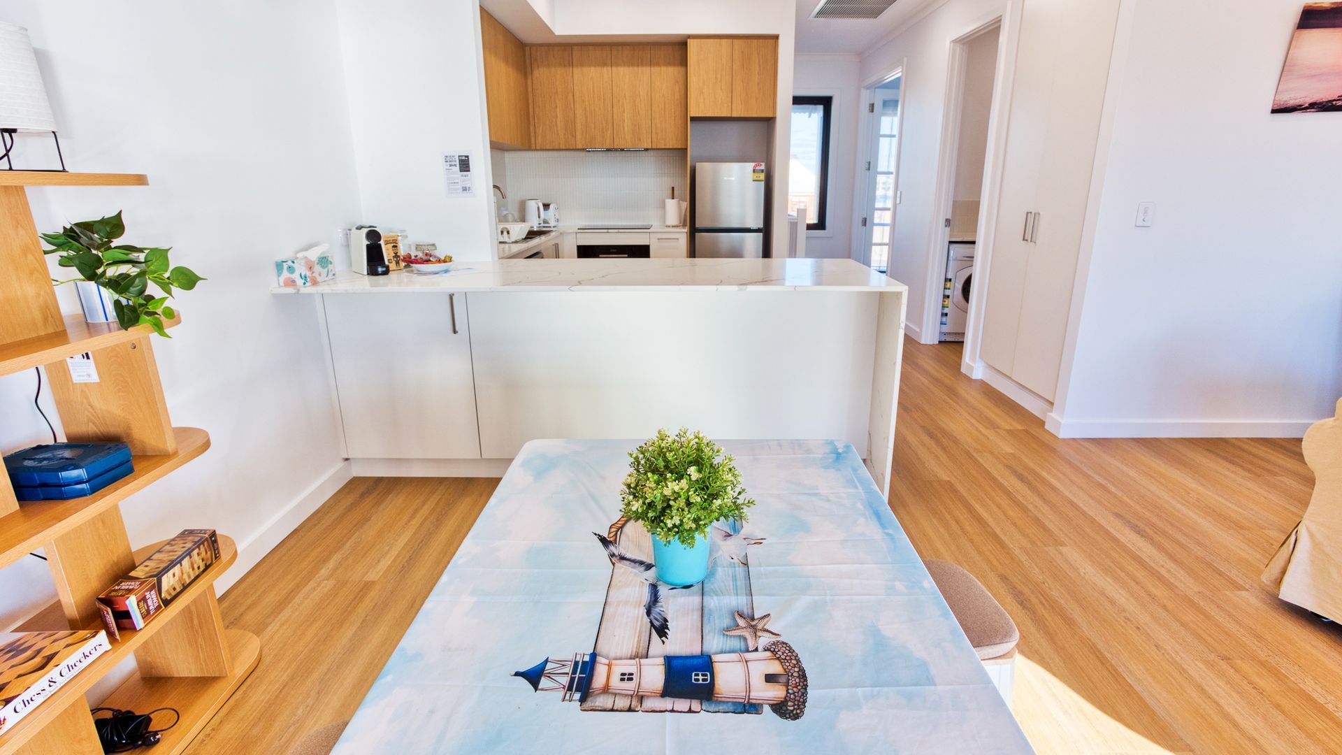 A modern kitchen with white cabinets, a stainless steel refrigerator, and a dining area with a wooden table and a blue rug featuring a nautical theme.