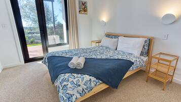 A bedroom with a large bed, a wooden nightstand, a glass coffee table, and a view of the outdoors.