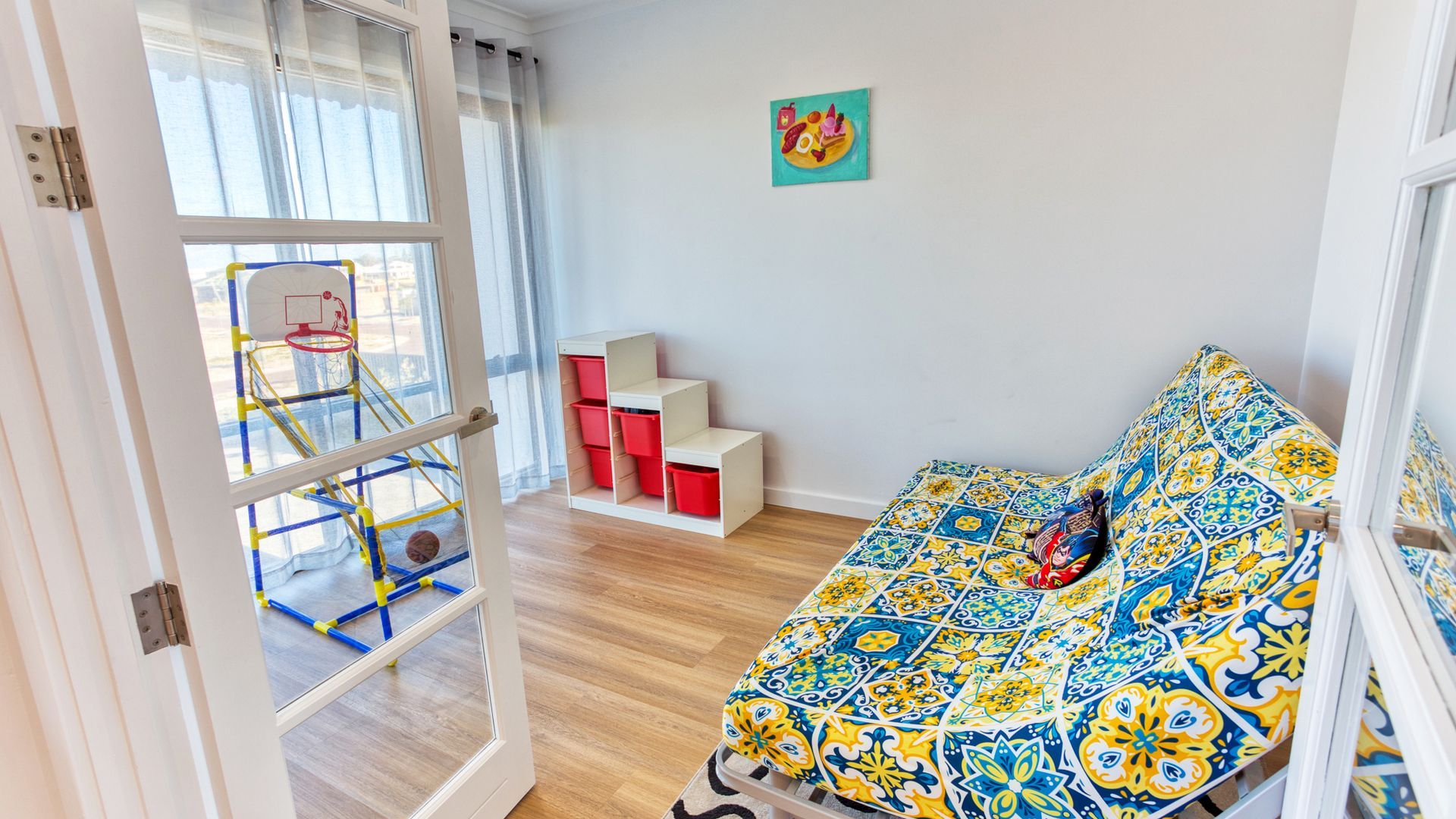 Een kamer met een bed, een raam met uitzicht op een basketbalring en een vrolijke wanddecoratie.