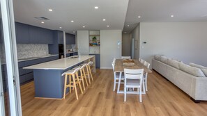 Eine moderne Küche mit Kochinsel, Barhocker und einem Essbereich mit Holztisch und weißen Stühlen.