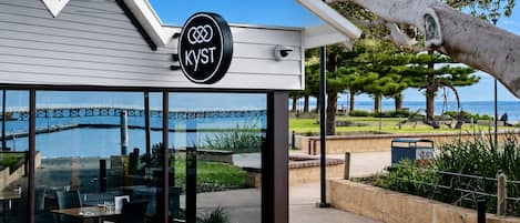 Een restaurant met uitzicht op het water en een brug, met een bord waarop het logo 'KYST' staat.