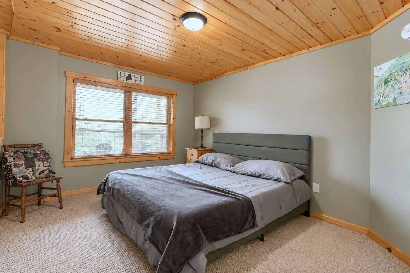 Un dormitorio con cama, mesita de noche, silla, ventana con persianas y lámpara de techo.