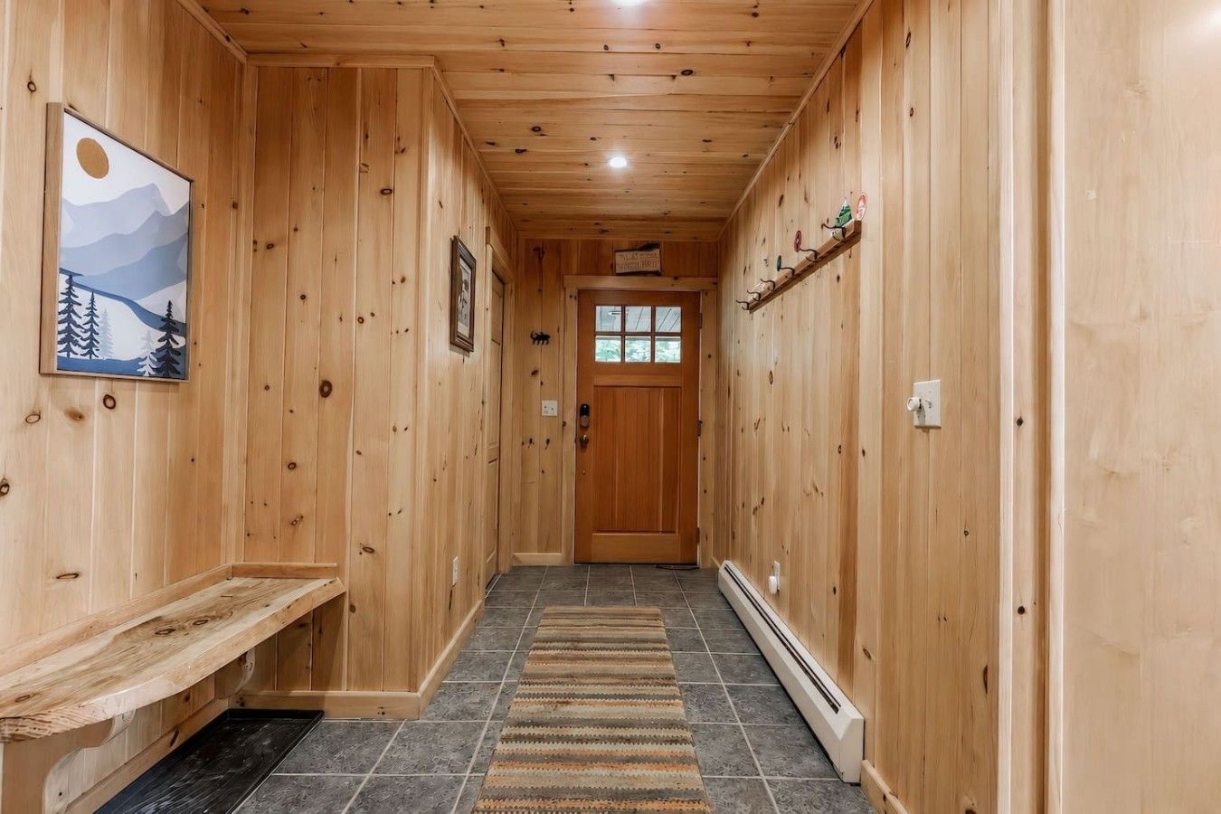 A wooden hallway with a bench, a rug, and a door at the end.