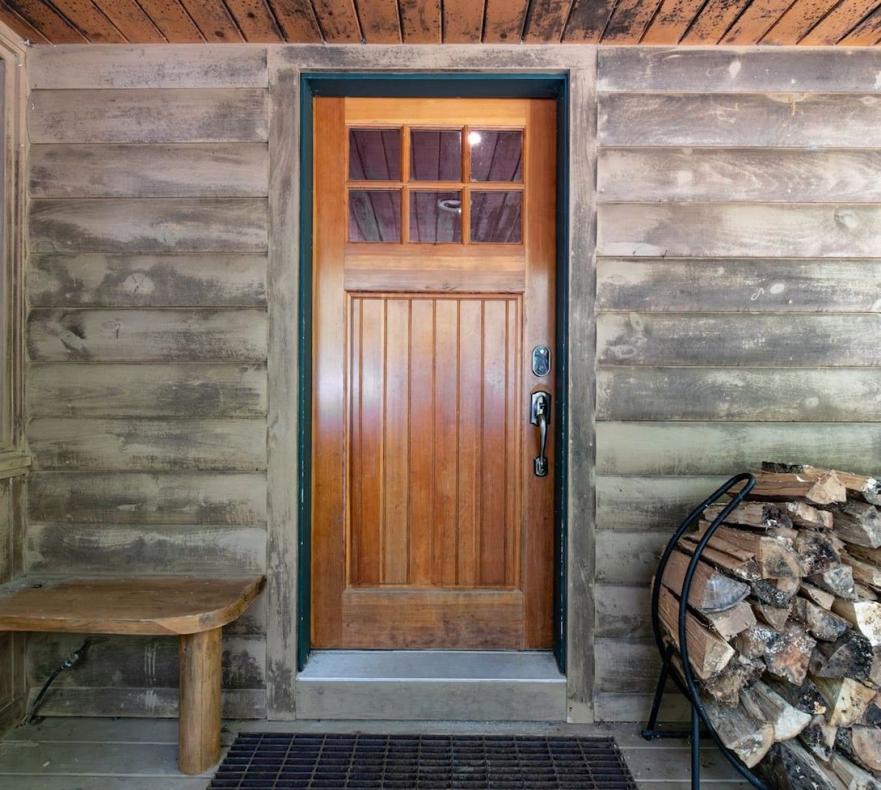 A wooden door with a window, a bench, and a stack of firewood.