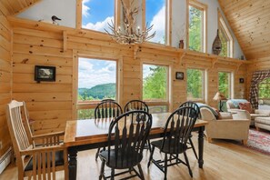A wooden cabin interior with a dining table, chairs, a chandelier, and large windows offering a view of the outdoors. - Sleeps 10, Lake View Retreat, with Hot tub & Barrel Sauna (Woodstock)