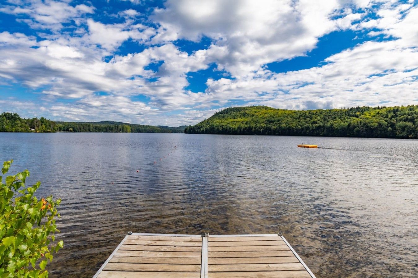 Une jetée en bois s’étendant sur un lac paisible, avec une colline boisée en arrière-plan.