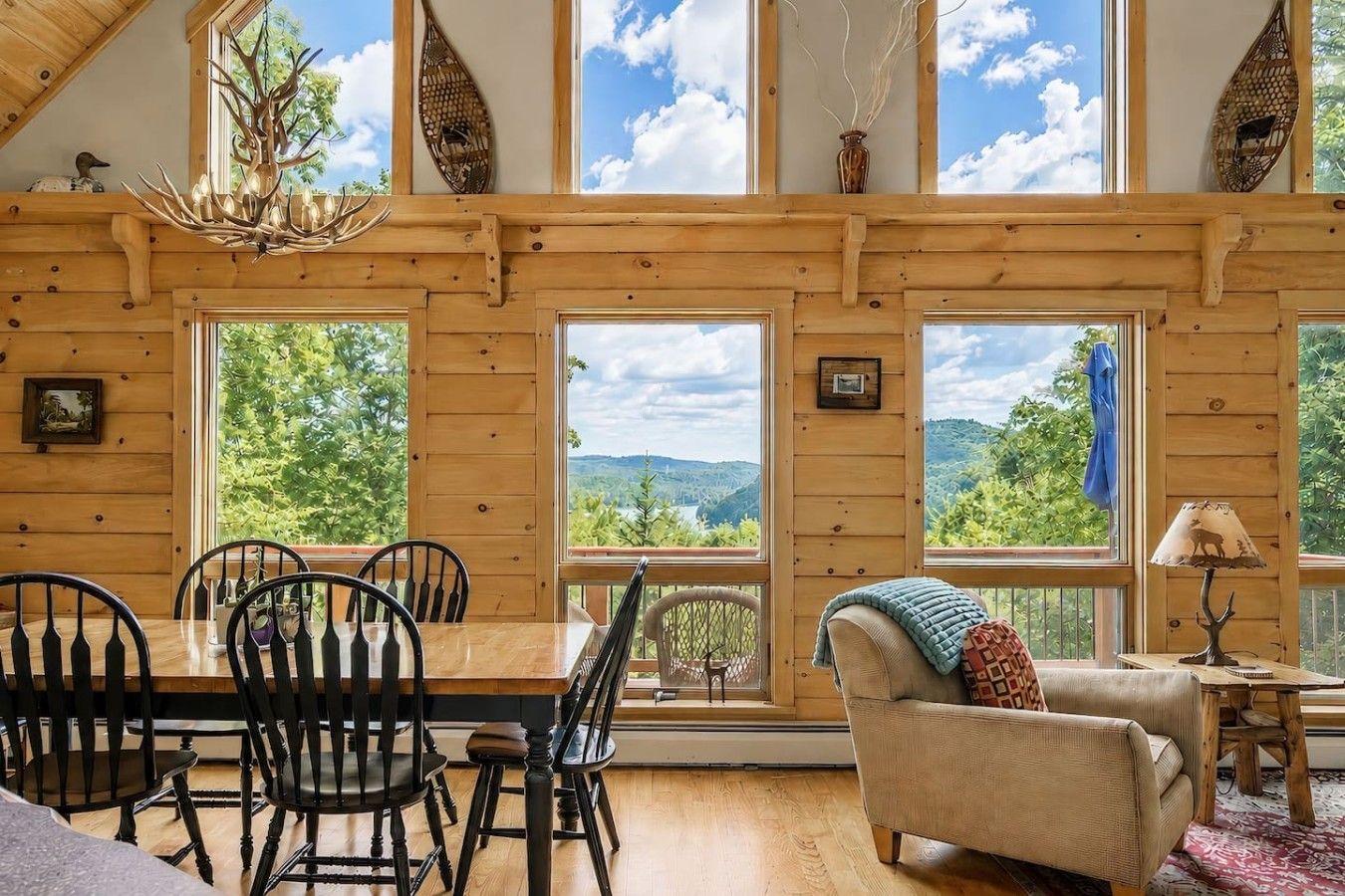 Un interior de madera con un comedor, un sofá y amplios ventanales que ofrecen vistas al exterior.