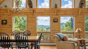Un interior de madera con un comedor, un sofá y amplios ventanales que ofrecen vistas al exterior.