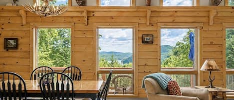 A wooden interior with a dining area, a sofa, and large windows offering a view of the outdoors.