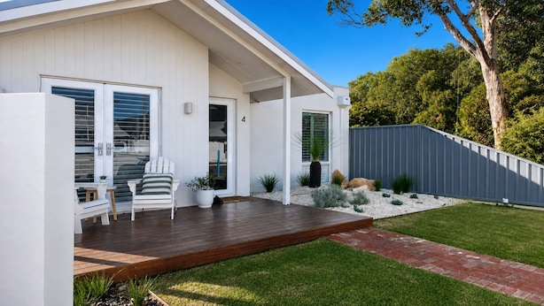 Een modern huis met een houten terras, een overdekte veranda en een verzorgd gazon.