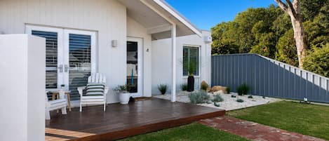 Une maison moderne dotée d’une terrasse en bois, d’un porche abrité et d’une pelouse bien entretenue.