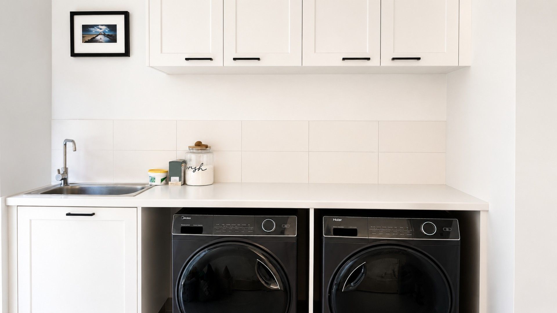 A compact kitchen with white cabinets, a sink, and two front-loading washing machines.