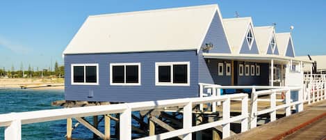 A waterfront wooden structure with multiple levels, a white railing, and a clear view of the water.