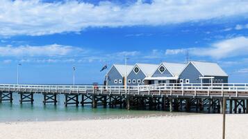 A pier with a building at the end, a sandy beach, and a clear blue sky.