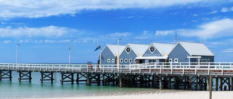A pier with a building at the end, a sandy beach, and a clear blue sky.
