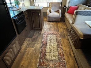 A compact living space with a kitchenette, a patterned rug, and a sofa. - PRIVATE COZY RV FOR RENT; ONLY 2 RVS ON PROPERTY, HOT TUB, CHARCOAL GRILL;SERENE (Canyon Lake)