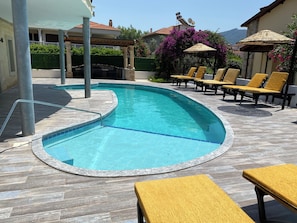 A swimming pool with a curved edge, surrounded by lounge chairs and a pergola.