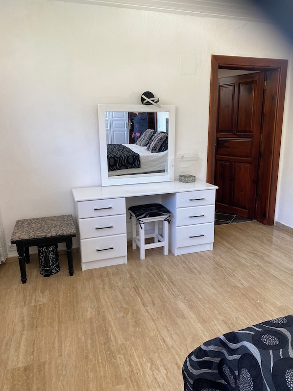 A room with a white desk, a mirror, a small stool, and a wooden door.