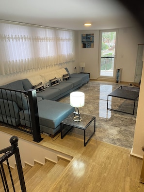 A living room with a sectional sofa, a coffee table, and a lamp. There is a staircase leading to another level.