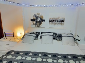 A bedroom with a bed, a bedside table with a lamp, and wall art.