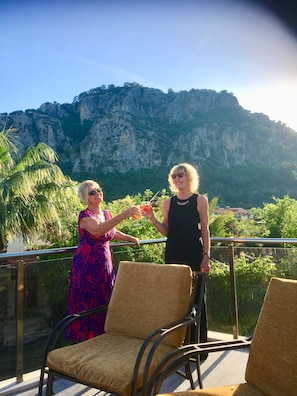 Two people on a balcony with chairs, overlooking a mountainous landscape.