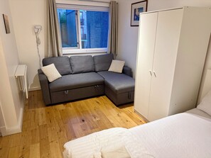 A room with a grey sectional sofa, a white wardrobe, and a bed with a white duvet. - The Oak Residence | En-Suite | Canada Water (London)