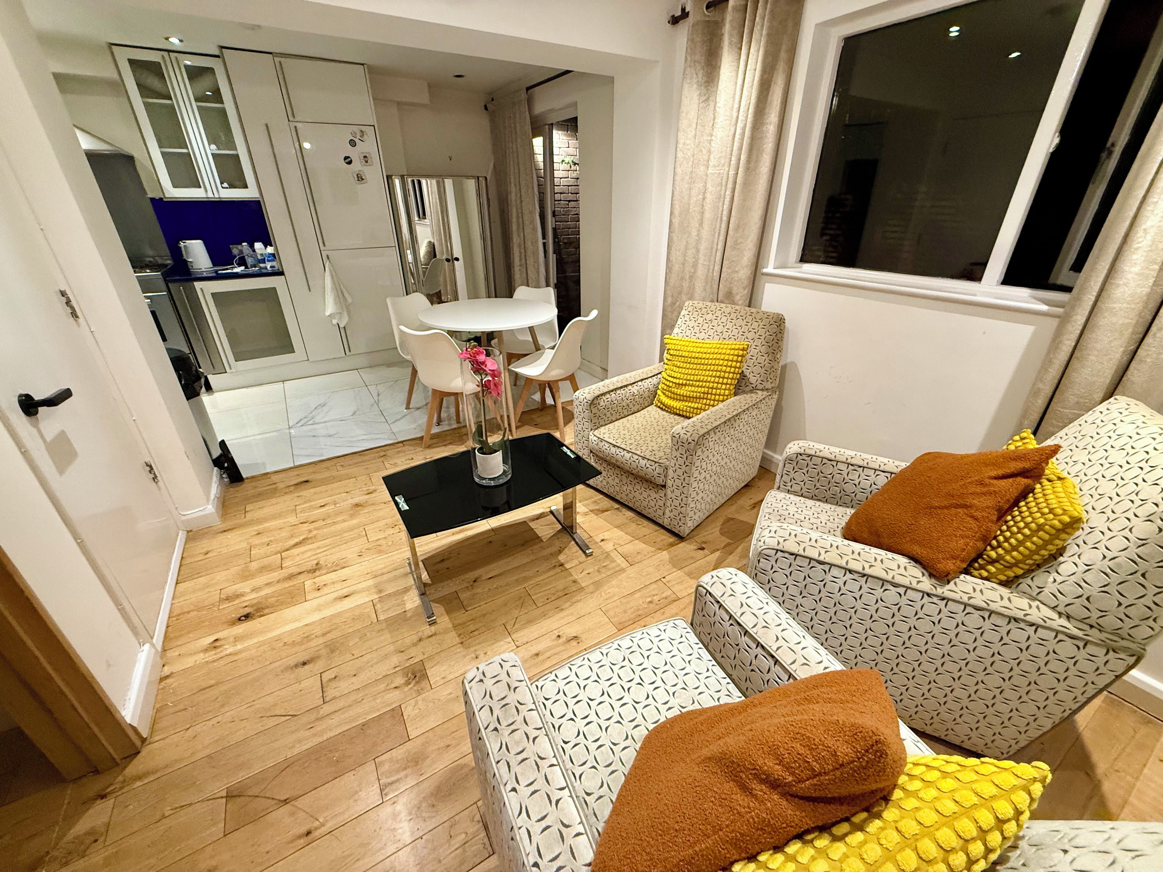 A modern living room with a dining area, a kitchen in the background, and a large window.