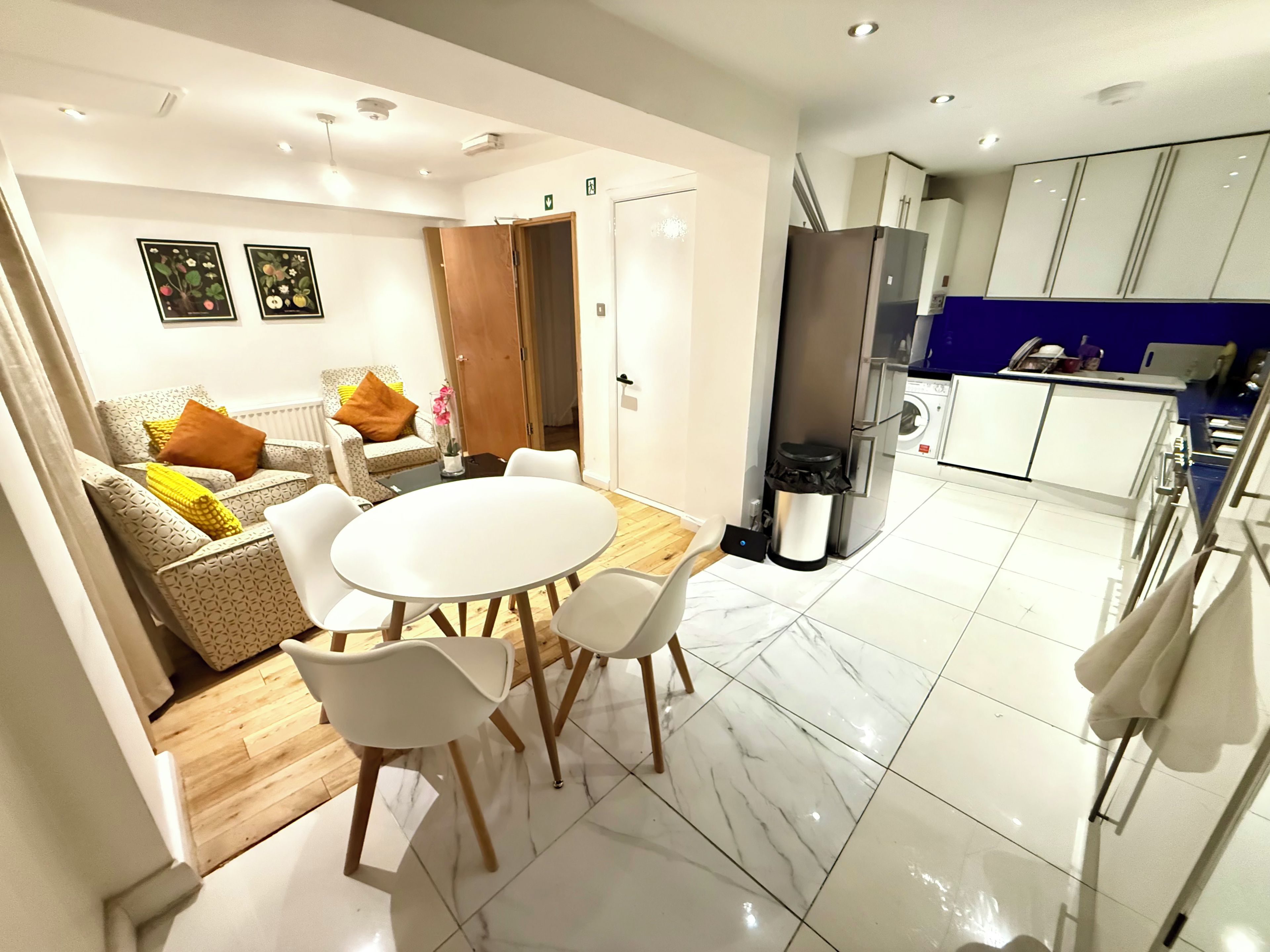 A modern kitchen with a refrigerator, stove, and sink. There is a dining area with a round table and chairs.