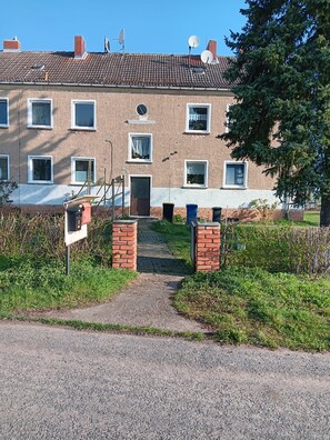 Ein zweistöckiges Gebäude mit Ziegelverkleidung, zahlreichen Fenstern und einem kleinen Vorgarten.