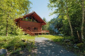 Eine Blockhütte mit einer Terrasse, umgeben von dichtem Wald.