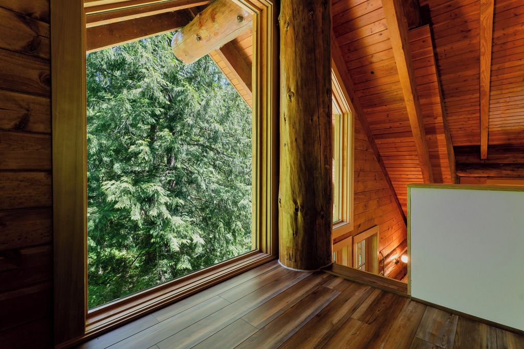 Interior de una cabaña de madera con un ventanal grande, vigas de madera y techo inclinado.