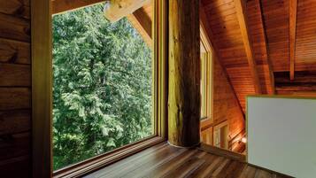Interior de una cabaña de madera con un ventanal grande, vigas de madera y techo inclinado.