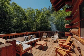 Eine Holzterrasse mit Gartenmöbeln, darunter eine Sitzecke und Stühle, umgeben von Bäumen.