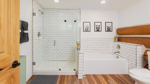 Ein Badezimmer mit einer gläsernen Duschkabine, einer weißen Badewanne, Holzboden und einem hölzernen Kopfteil.