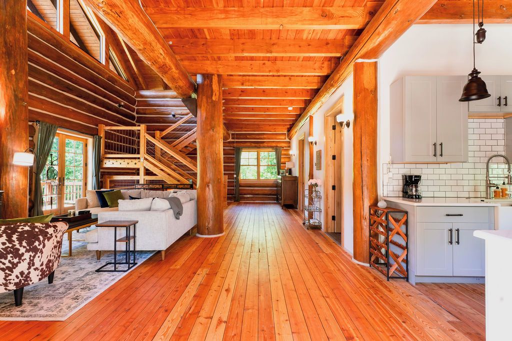 Interior de una cabaña de madera con piso de madera, un sofá, un comedor y una cocina con gabinetes blancos.