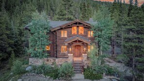 A log cabin with a stone foundation, a wooden front door, and a staircase leading to the entrance. - Luxury w/ River Views + Hot Tub + Private Shuttle - Rivertree Lodge (Breckenridge)